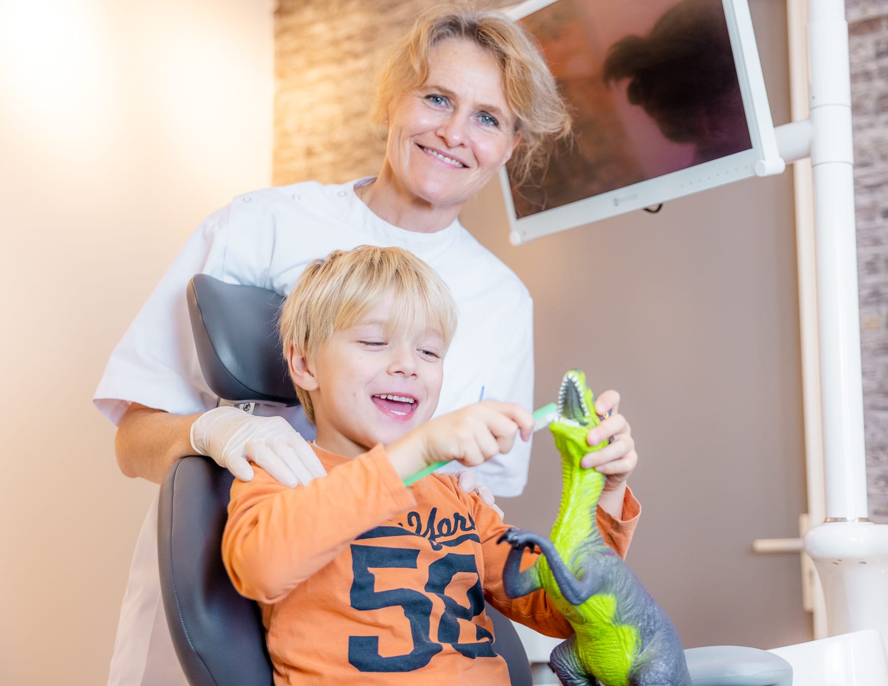 Mondhygiënist behandelt kind met speelgoeddino tijdens controle